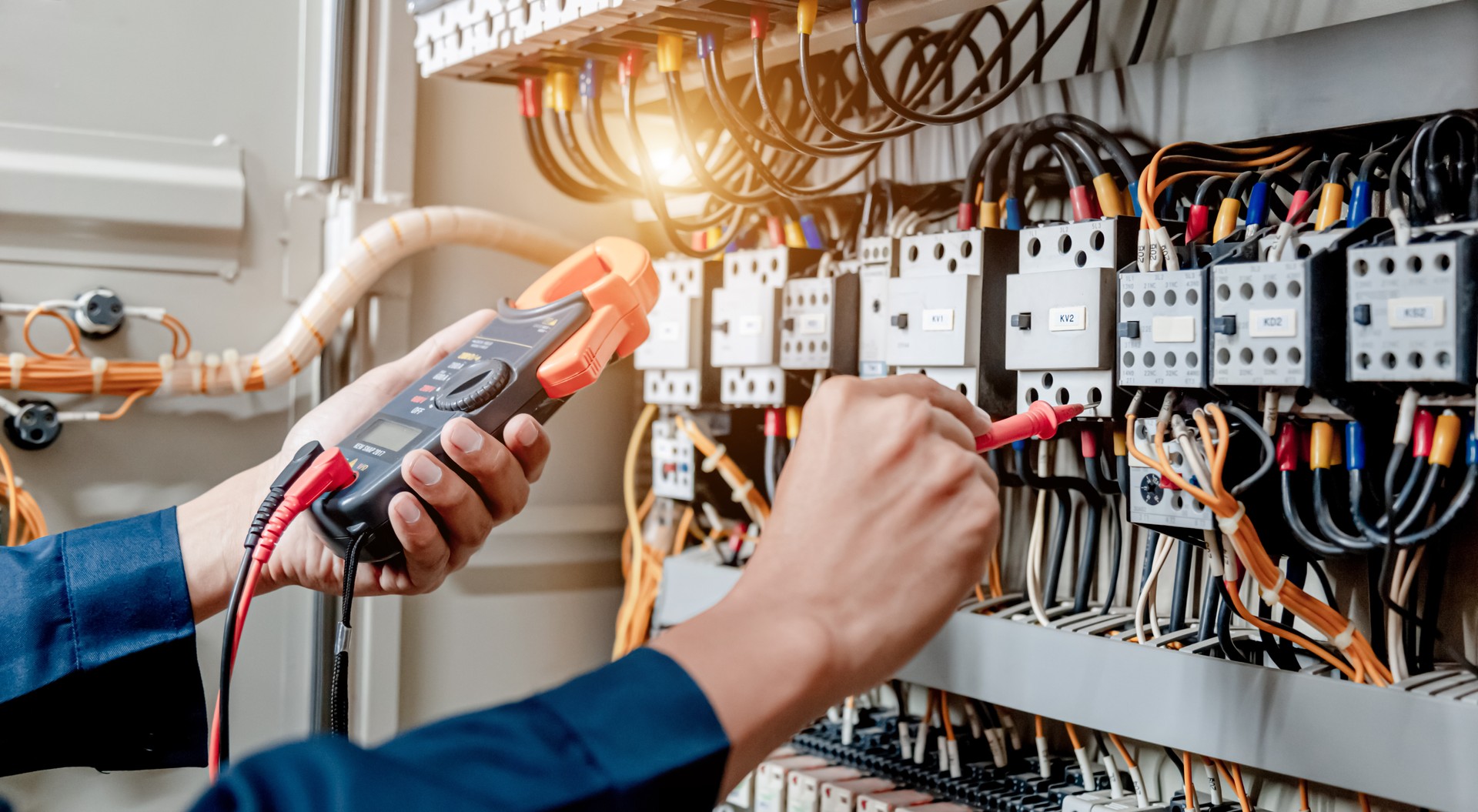 Electrician engineer uses a multimeter to test the electrical installation and power line current in an electrical system control cabinet.